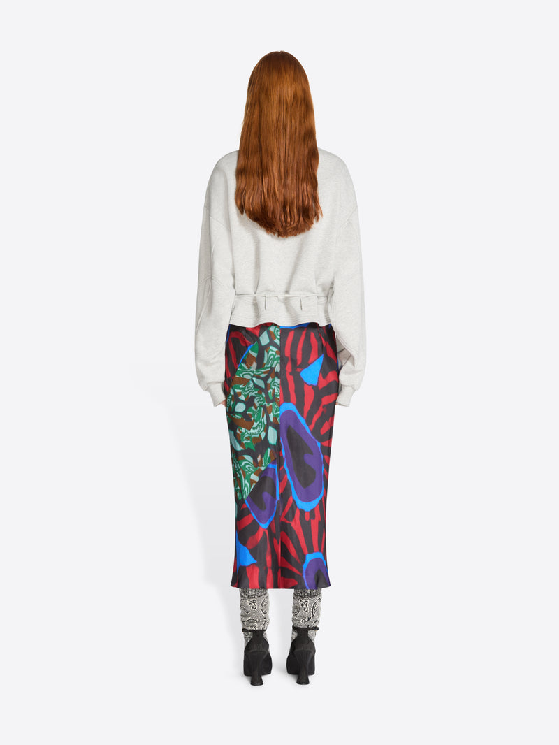 Back view of a person wearing a colorful skirt with abstract patterns and light gray sweatshirt on a white background