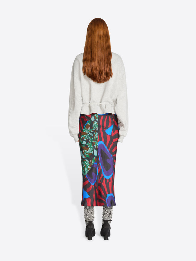 Back view of a person wearing a colorful skirt with abstract patterns and light gray sweatshirt on a white background
