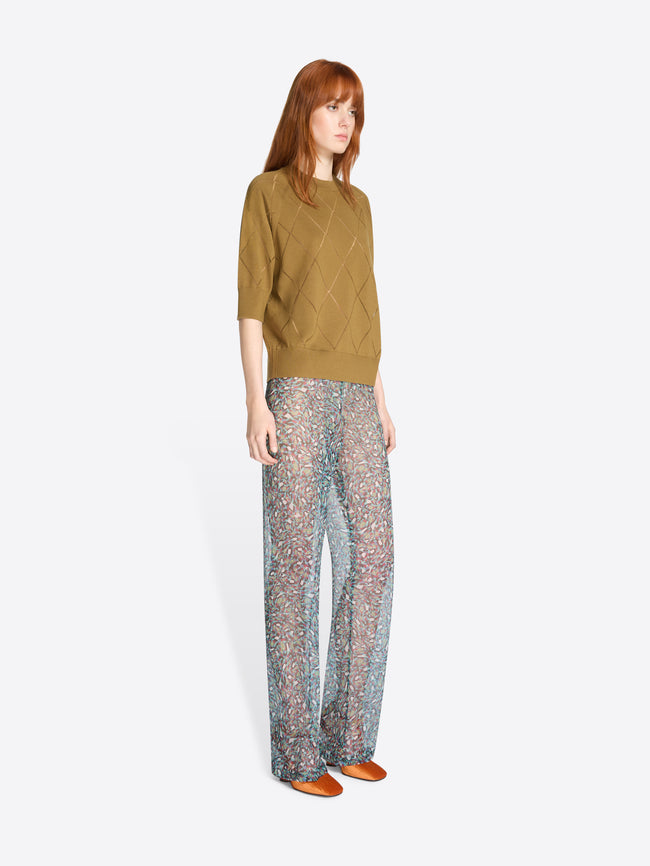 Woman wearing a mustard yellow knit top and patterned pants on a white background