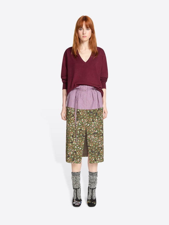 Woman wearing a burgundy sweater and patterned skirt on a white background
