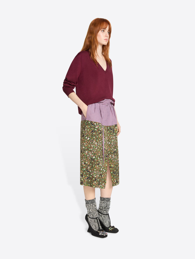 Woman wearing a burgundy sweater and green patterned skirt on a white background