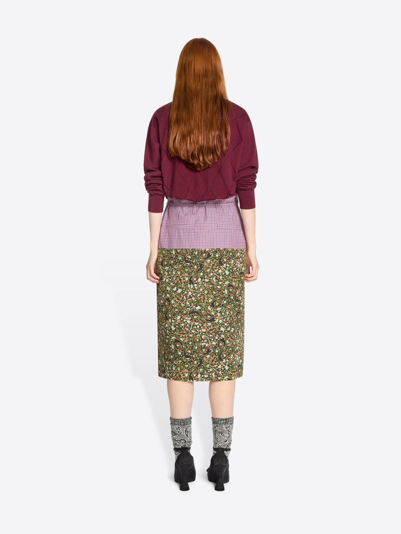 Back view of a person wearing a burgundy sweater and green floral skirt on a white background