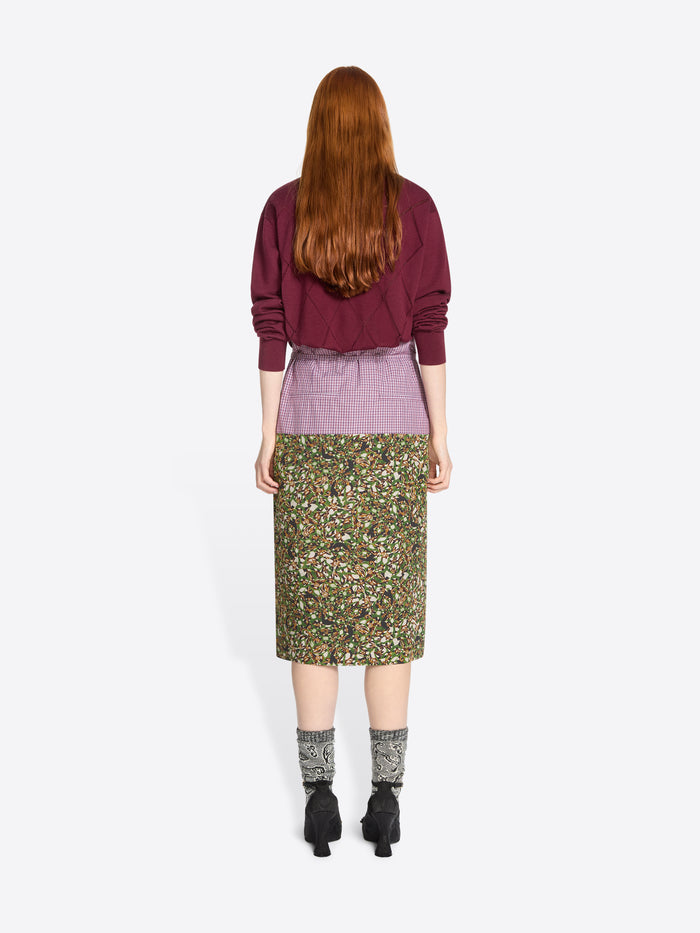 Back view of a person wearing a burgundy sweater and green floral skirt on a white background