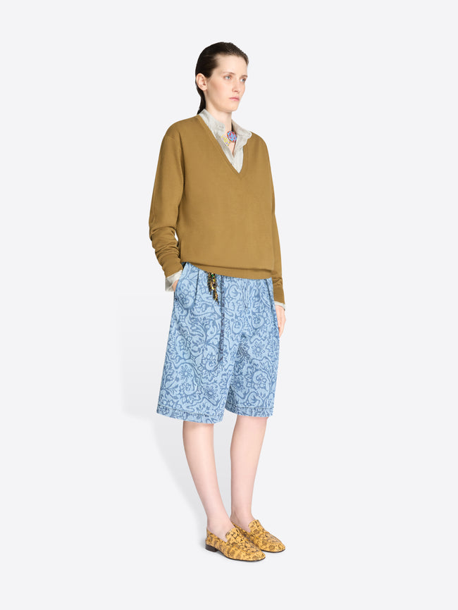 Woman wearing a mustard sweater and blue patterned shorts on a white background