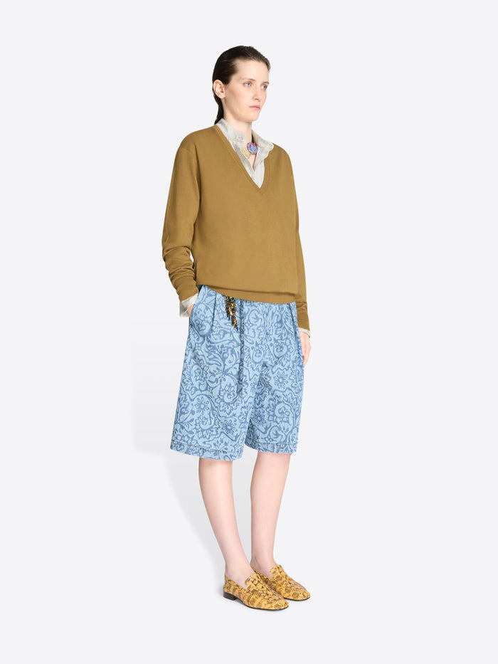 Woman wearing a mustard sweater and blue patterned shorts on a white background
