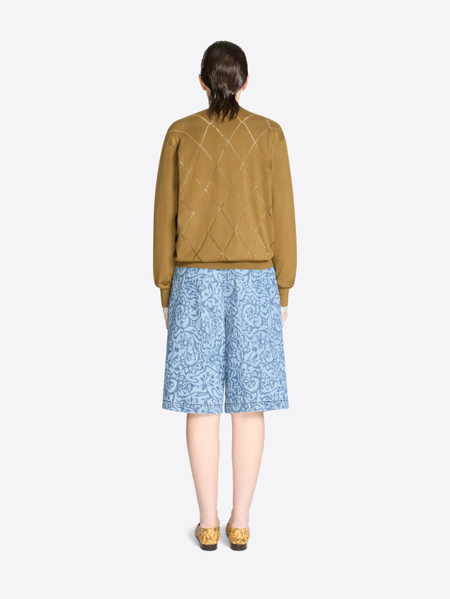 Back view of a person wearing a mustard yellow sweater and blue patterned shorts on a white background