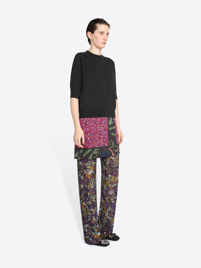 Person wearing a black top, skirt and colorful patterned pants on a white background