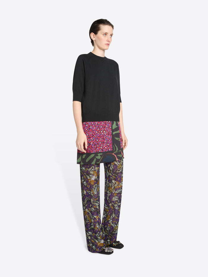 Person wearing a black top, skirt and colorful patterned pants on a white background