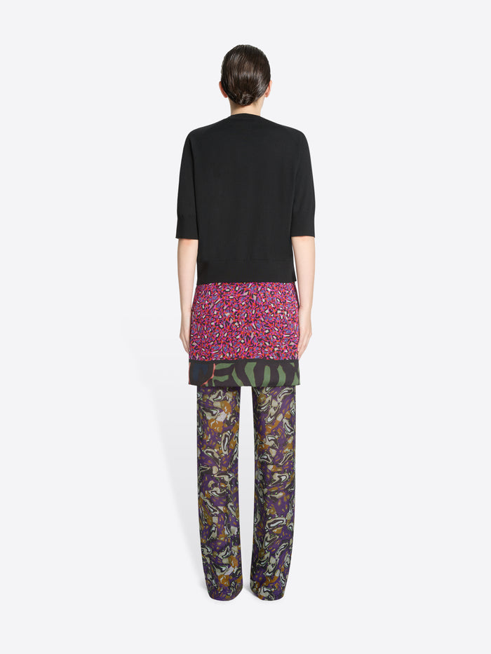 Back view of a person wearing a black top, skirt and patterned pants on a white background