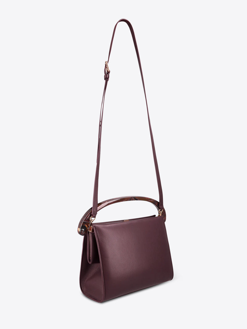 Burgundy leather handbag with a strap on a white background
