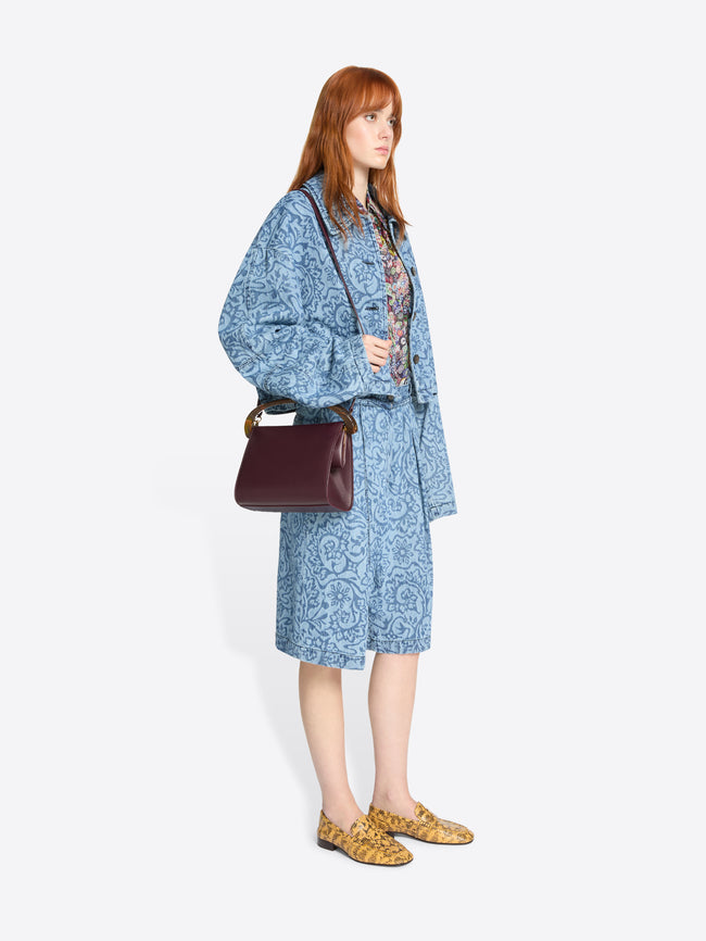 Woman wearing a blue patterned outfit with a burgundy bag on a white background