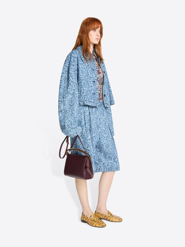 Woman wearing a blue patterned outfit with a burgundy handbag on a white background
