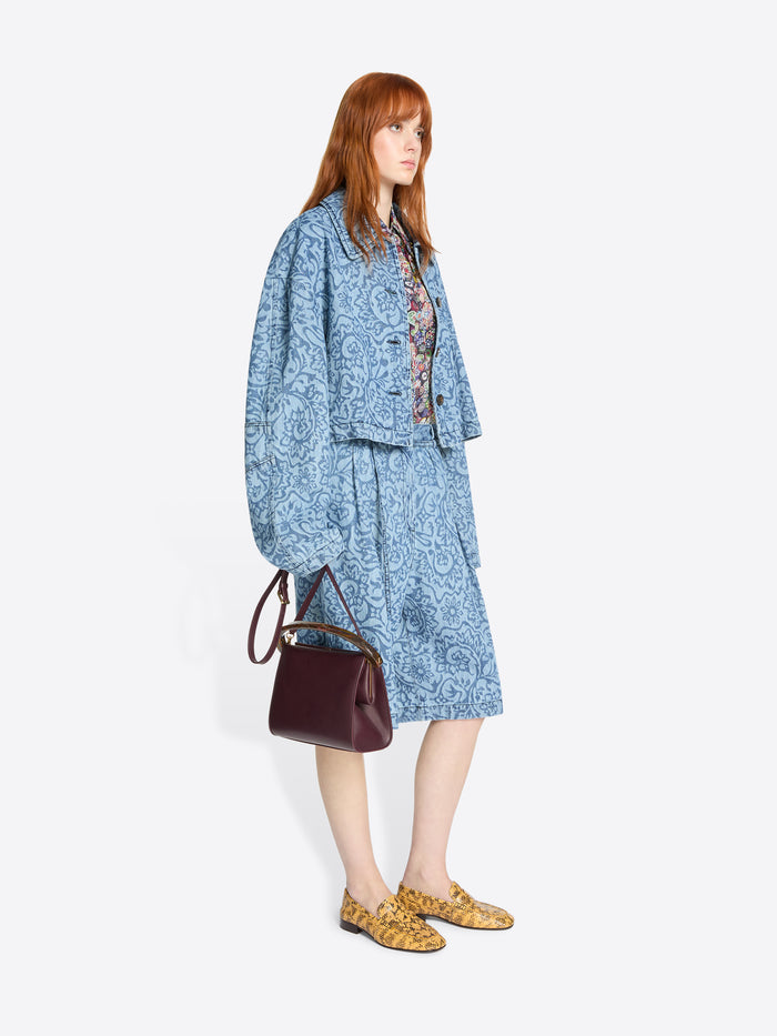 Woman wearing a blue patterned outfit with a burgundy handbag on a white background