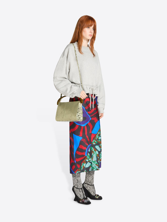 Woman wearing a light gray sweatshirt and colorful skirt with a bag on a white background