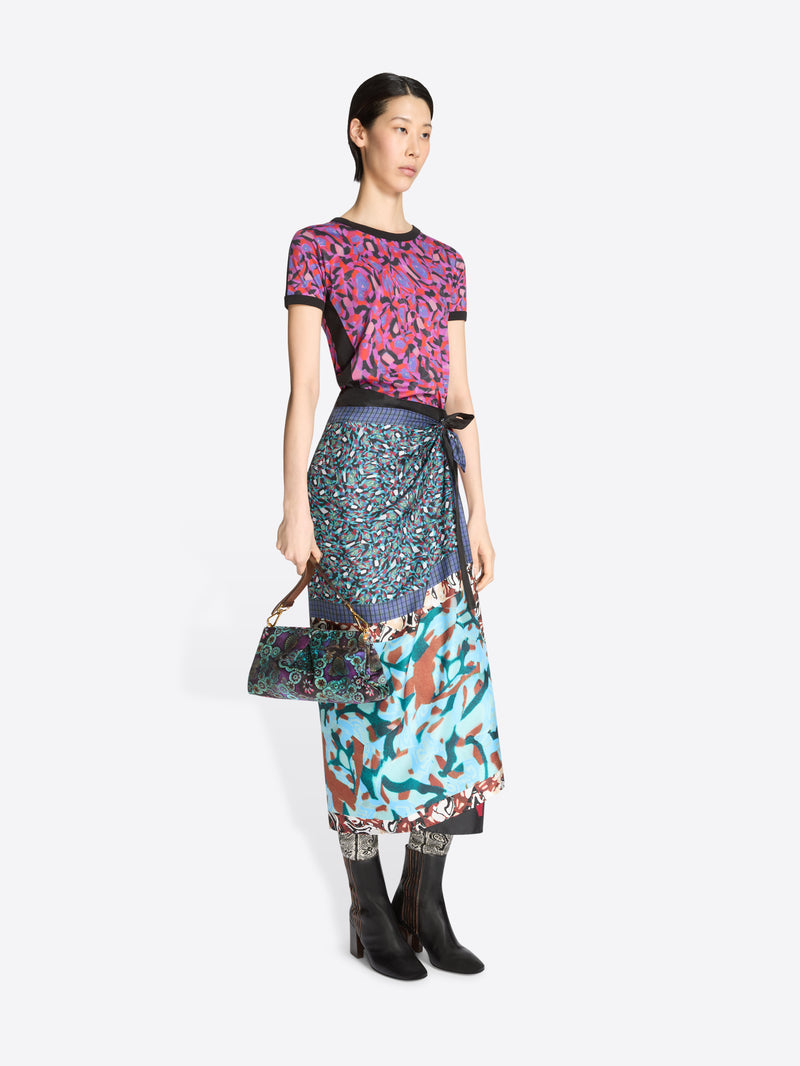 Woman wearing a colorful outfit with a patterned top and skirt, holding a matching handbag on a white background