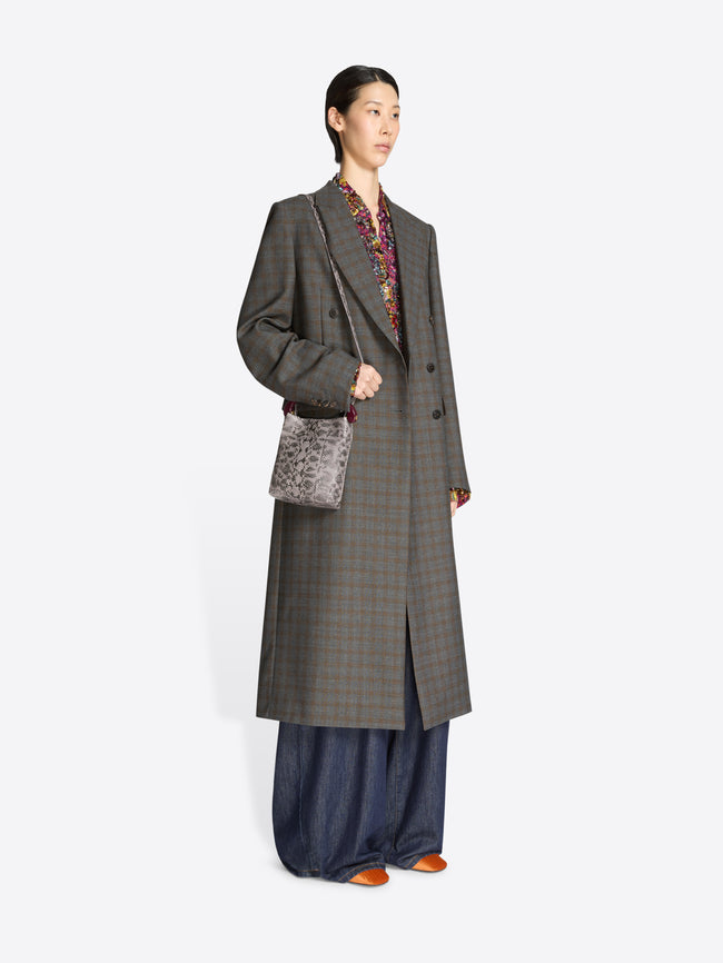 Woman wearing a long gray checkered coat with a snake print handbag on a white background