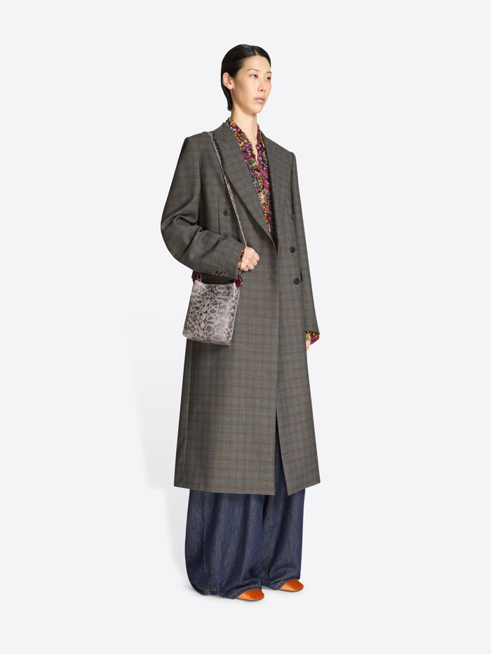 Woman wearing a long gray checkered coat with a snake print handbag on a white background