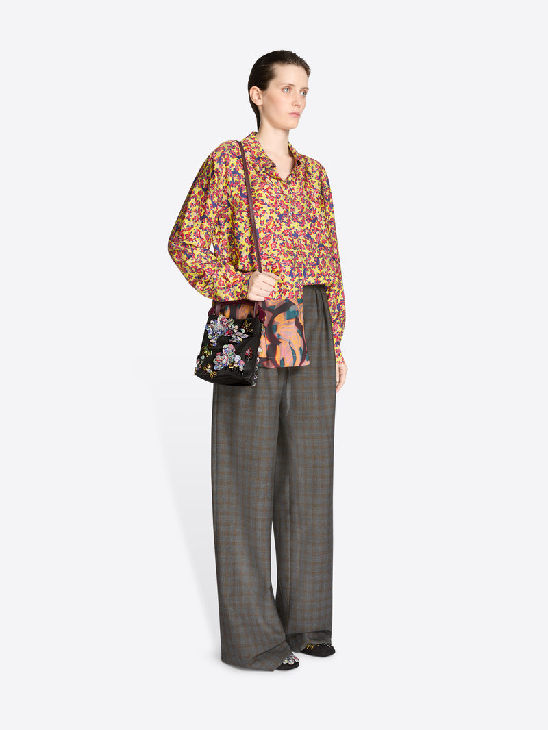 Woman wearing a colorful floral blouse and gray checkered pants with a handbag on a white background
