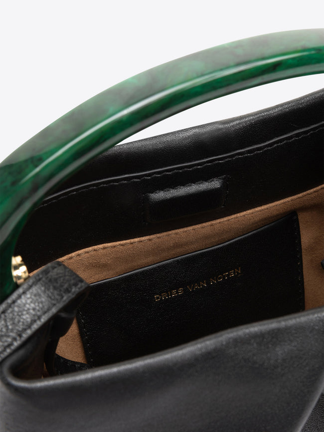 Close-up of a black leather handbag with a glossy green curved handle and a black interior label reading DRIES VAN NOTEN.