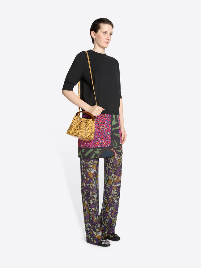 Woman wearing a black top, skirt and colorful pants, holding a bag on a white background
