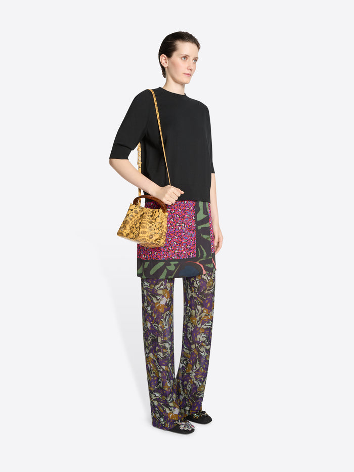 Woman wearing a black top, skirt and colorful pants, holding a bag on a white background