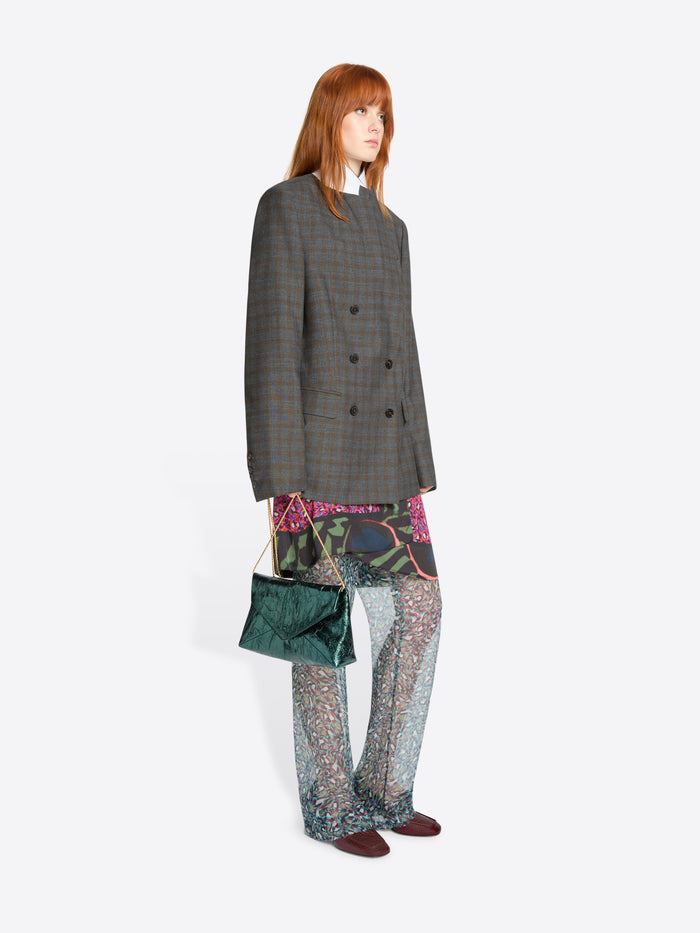 Woman wearing a gray checkered coat and patterned pants, holding a green handbag on a white background