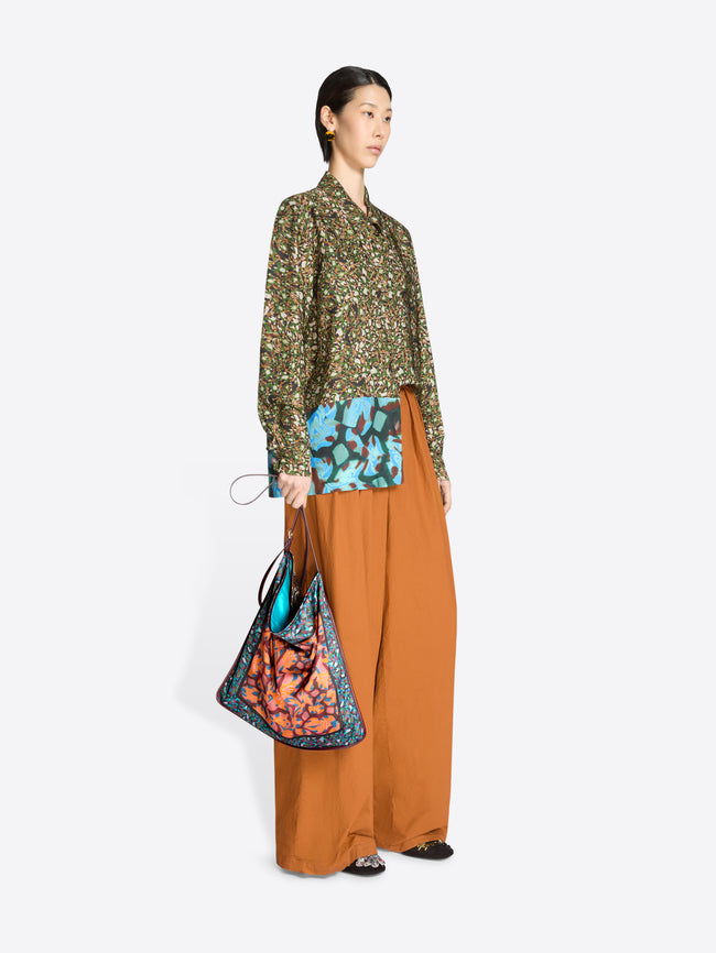 Woman holding a colorful bag wearing a patterned shirt and orange pants on a white background