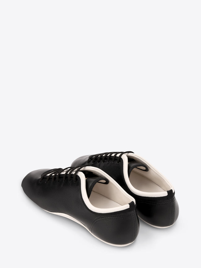 Pair of black sneakers with black laces on a light gray background