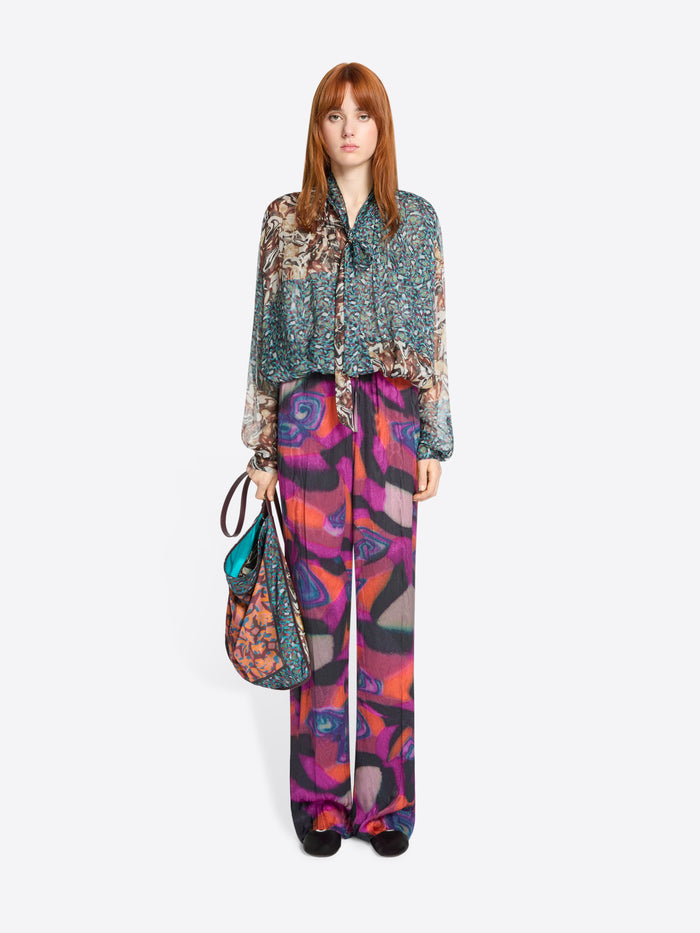 Woman wearing a patterned shirt and colorful pants with a handbag on a white background