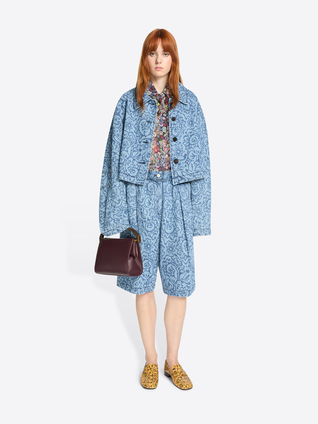 Woman wearing a blue patterned outfit and yellow patterned loafers with a burgundy handbag on a white background