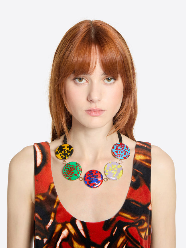 Woman wearing a colorful necklace with a patterned top on a white background