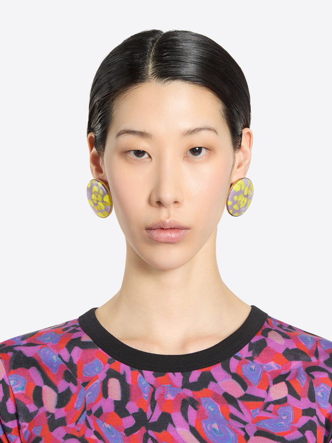 Person wearing statement earrings and a patterned shirt against a plain background