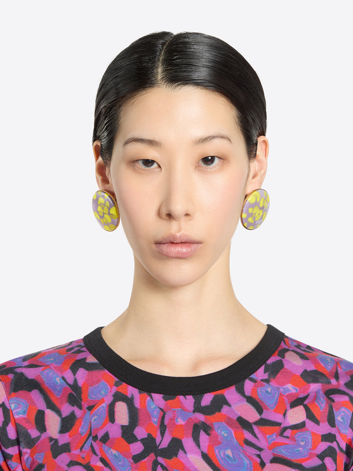 Person wearing statement earrings and a patterned shirt against a plain background