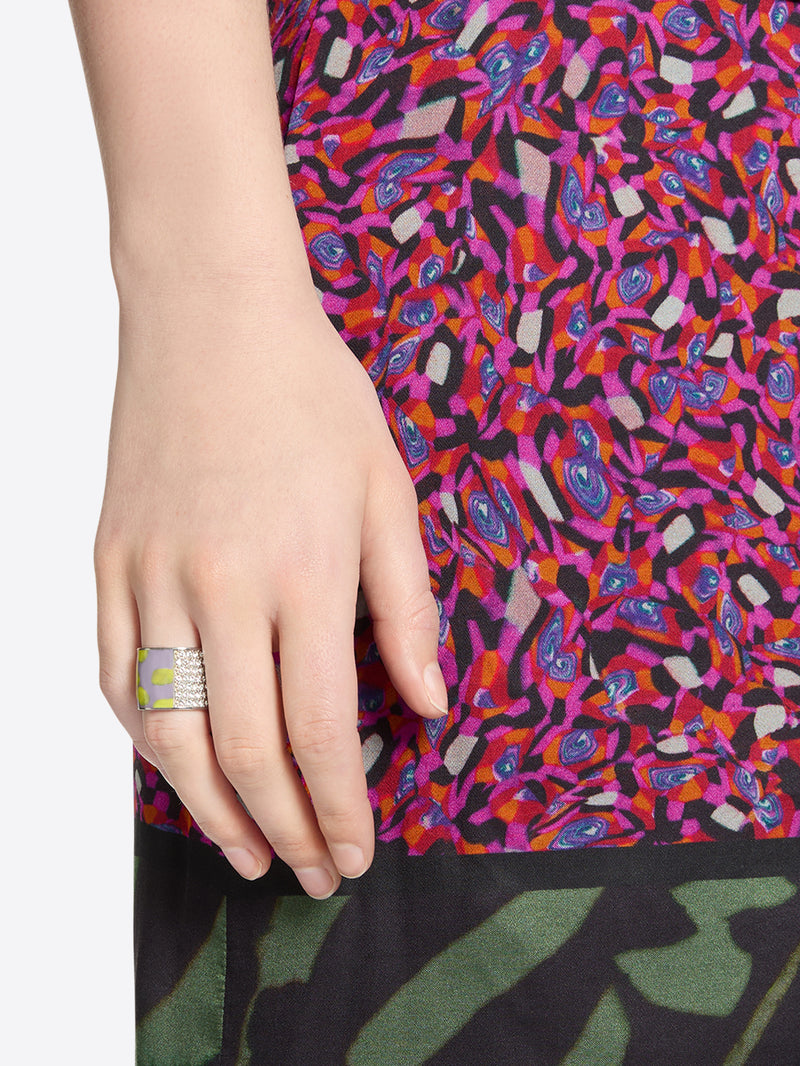 Close-up of a hand wearing a statement ring with sparkling crystals and a purple-yellow abstract pattern 