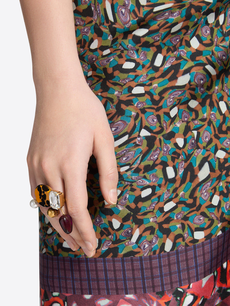 Close-up of a hand wearing a statement ring with a yellow patterned accent, faceted purple gemstone, clear crystal detail and pearl embellishment 