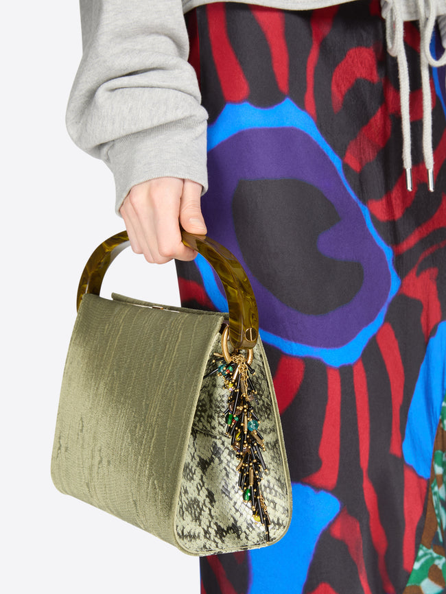 Person holding a green handbag with a colorful patterned garment in the background