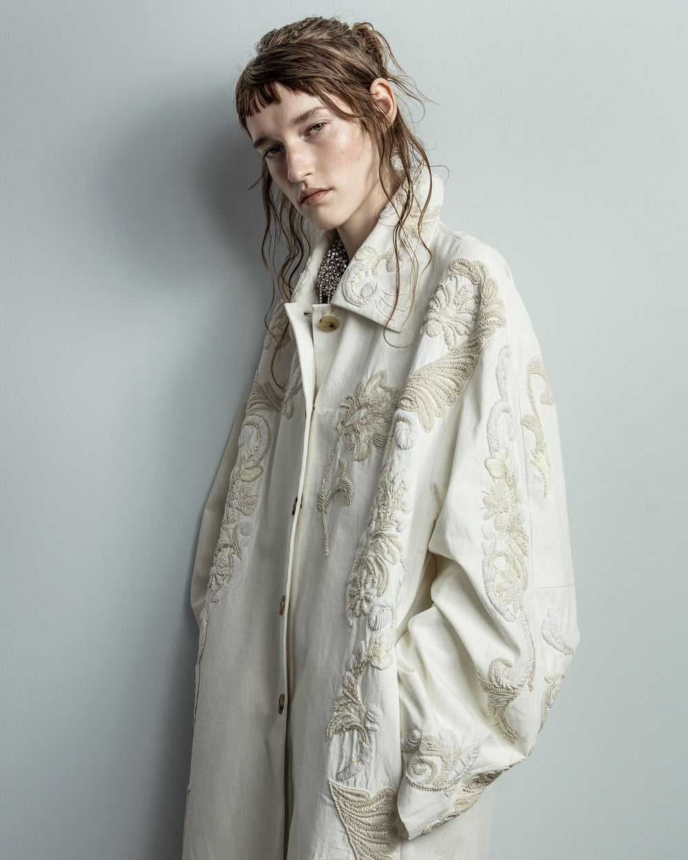 Person wearing a white coat with intricate patterns against a plain background - Dries Van Noten