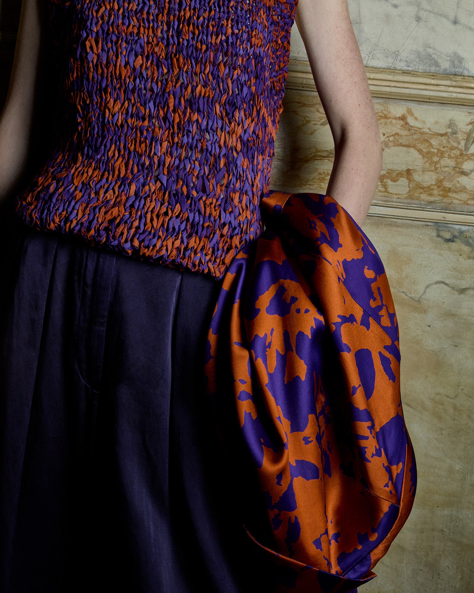 Person wearing a colorful patterned top against a textured wall.