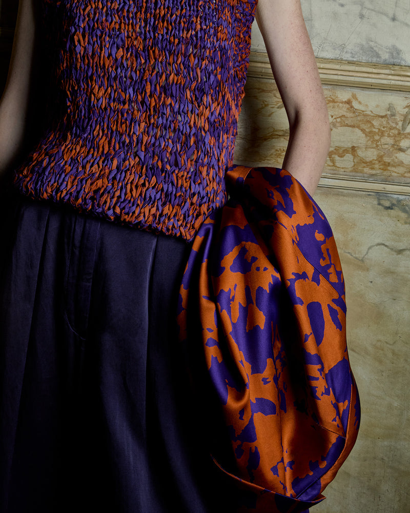 Person wearing a colorful patterned top against a textured wall. - Dries Van Noten