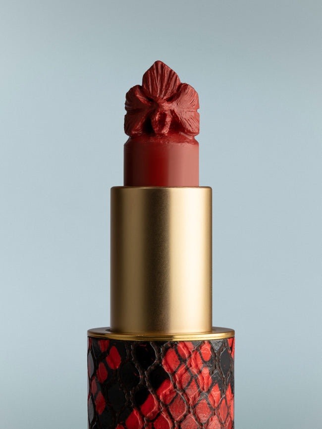 Lipstick with a decorative red and gold cap on a gray background