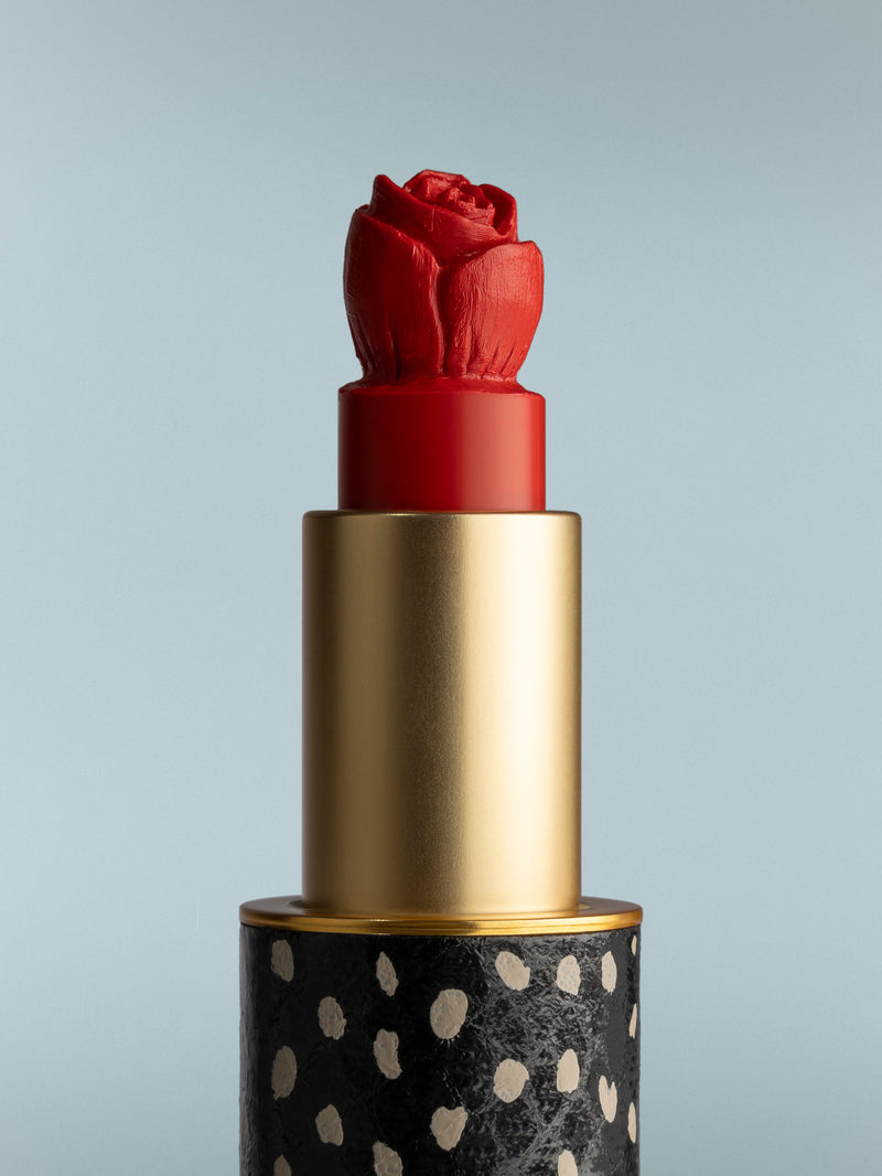 Red lipstick with a gold cap and black base featuring white polka dots on a gray background