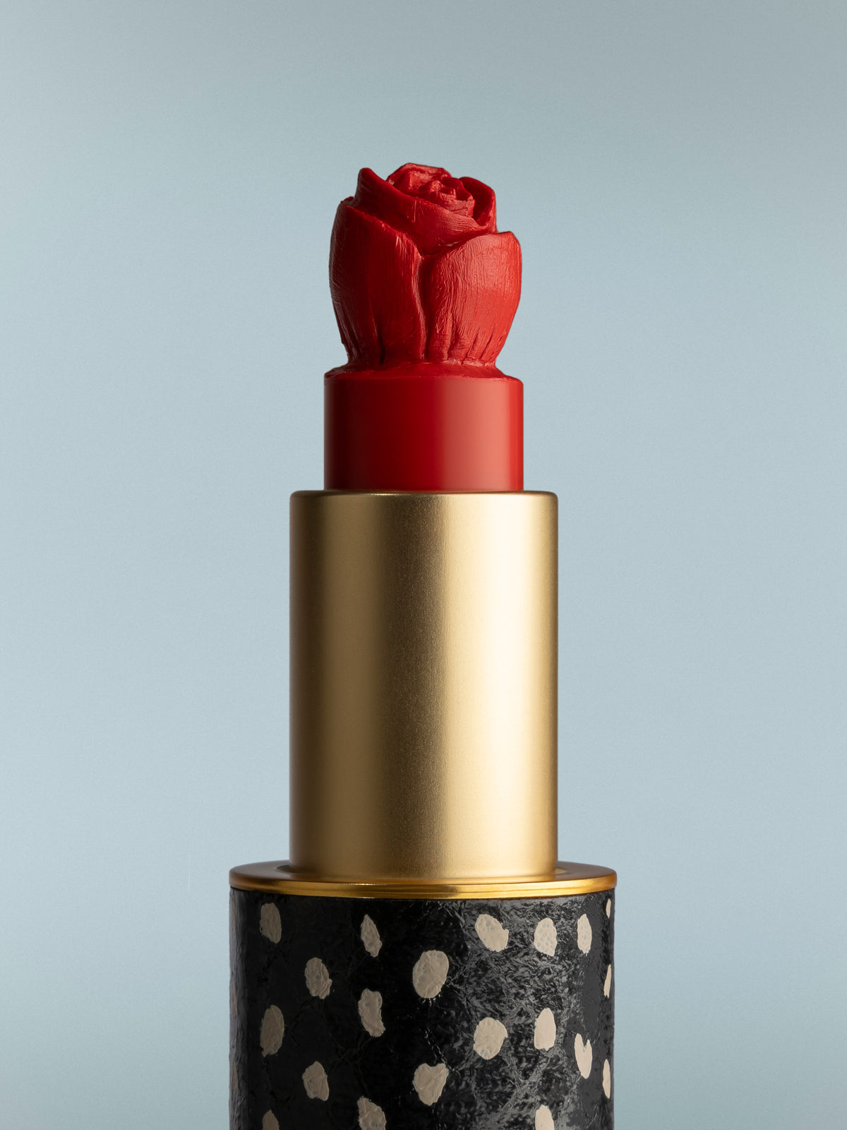 Red lipstick with a gold cap and black base featuring white polka dots on a gray background