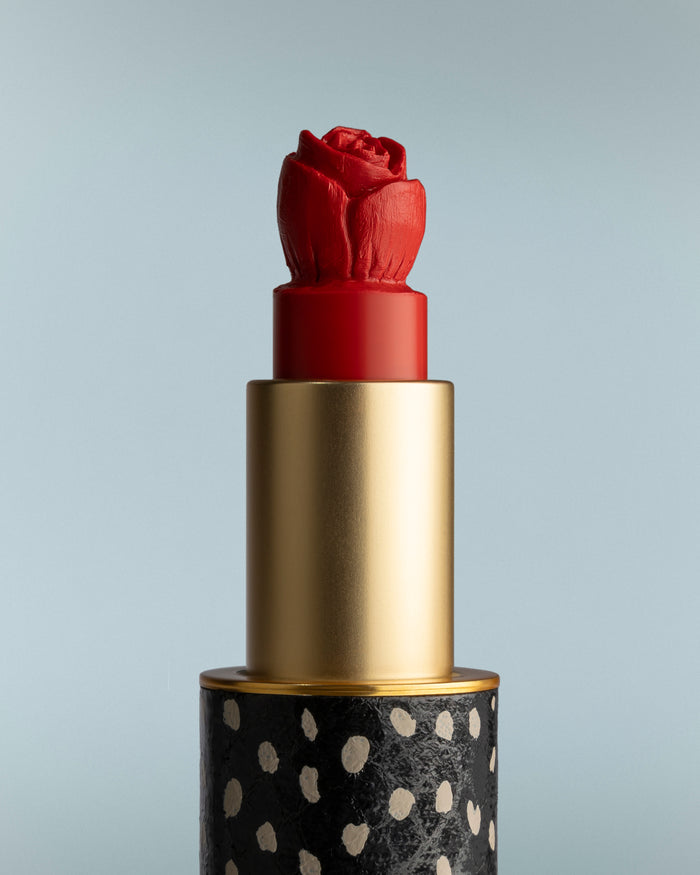 Red lipstick with a gold cap and black base featuring white polka dots on a gray background