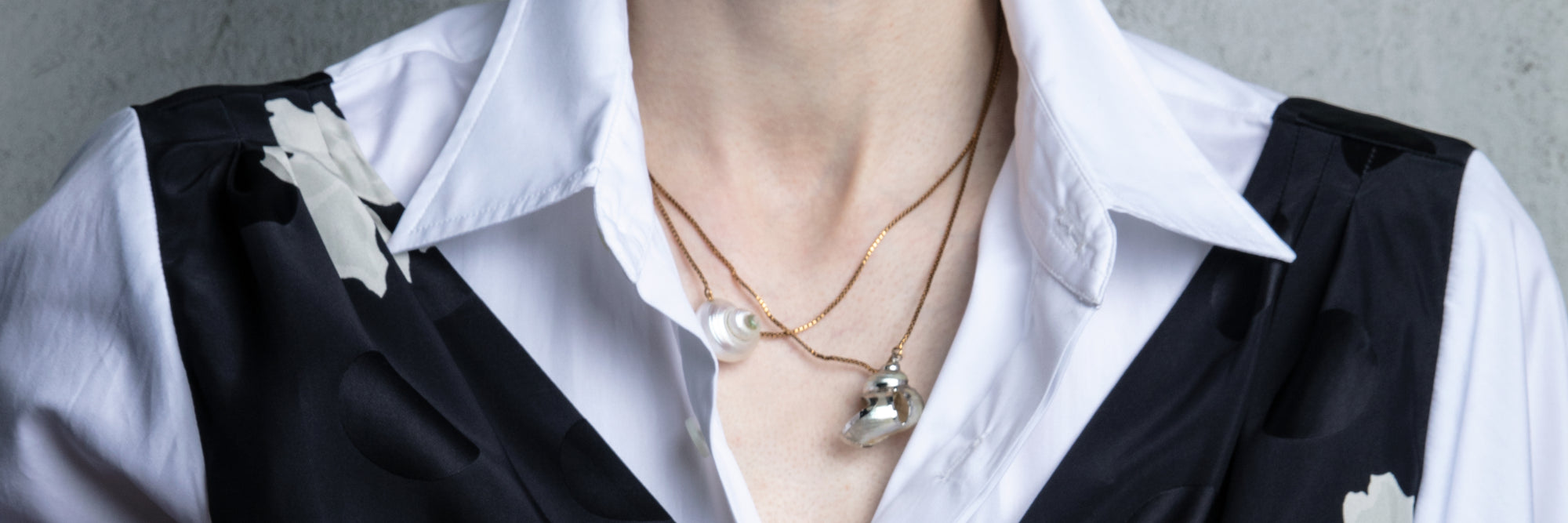 Person wearing a white shirt with black vest and floral details, accessorized with necklaces - Dries Van Noten
