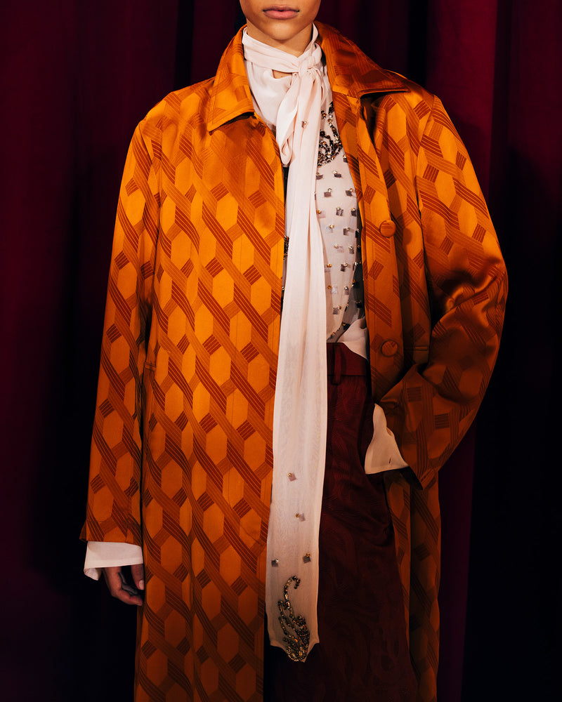 Person wearing an orange patterned coat with a white scarf against a dark background