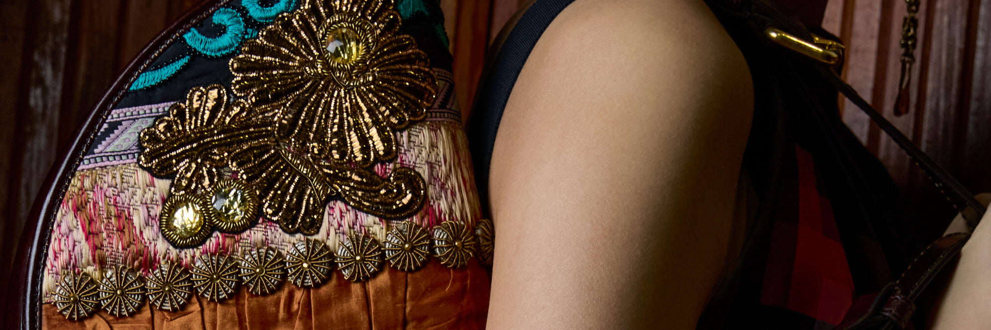 Close-up of a person wearing a black sleeveless top with a highly decorative, ornate gold embroidered bag featuring sequins and metallic detailing.