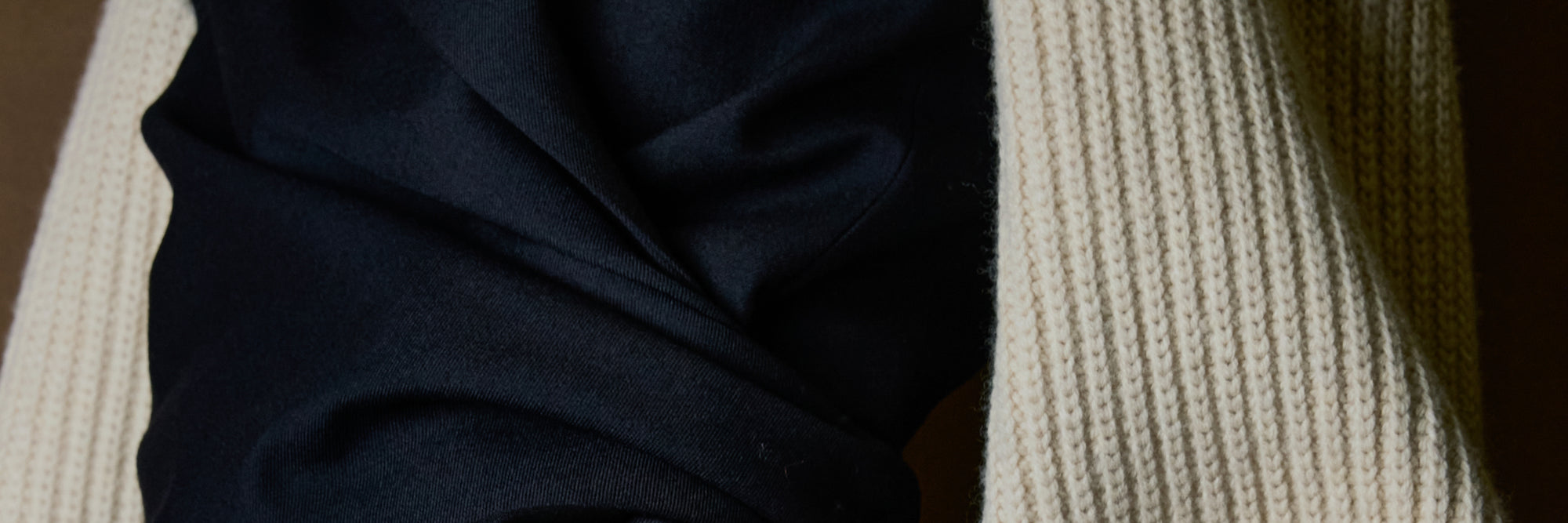 A close-up of a dark navy blue blazer with a cream ribbed knit sleeves, showing the texture and color contrast of the materials.
