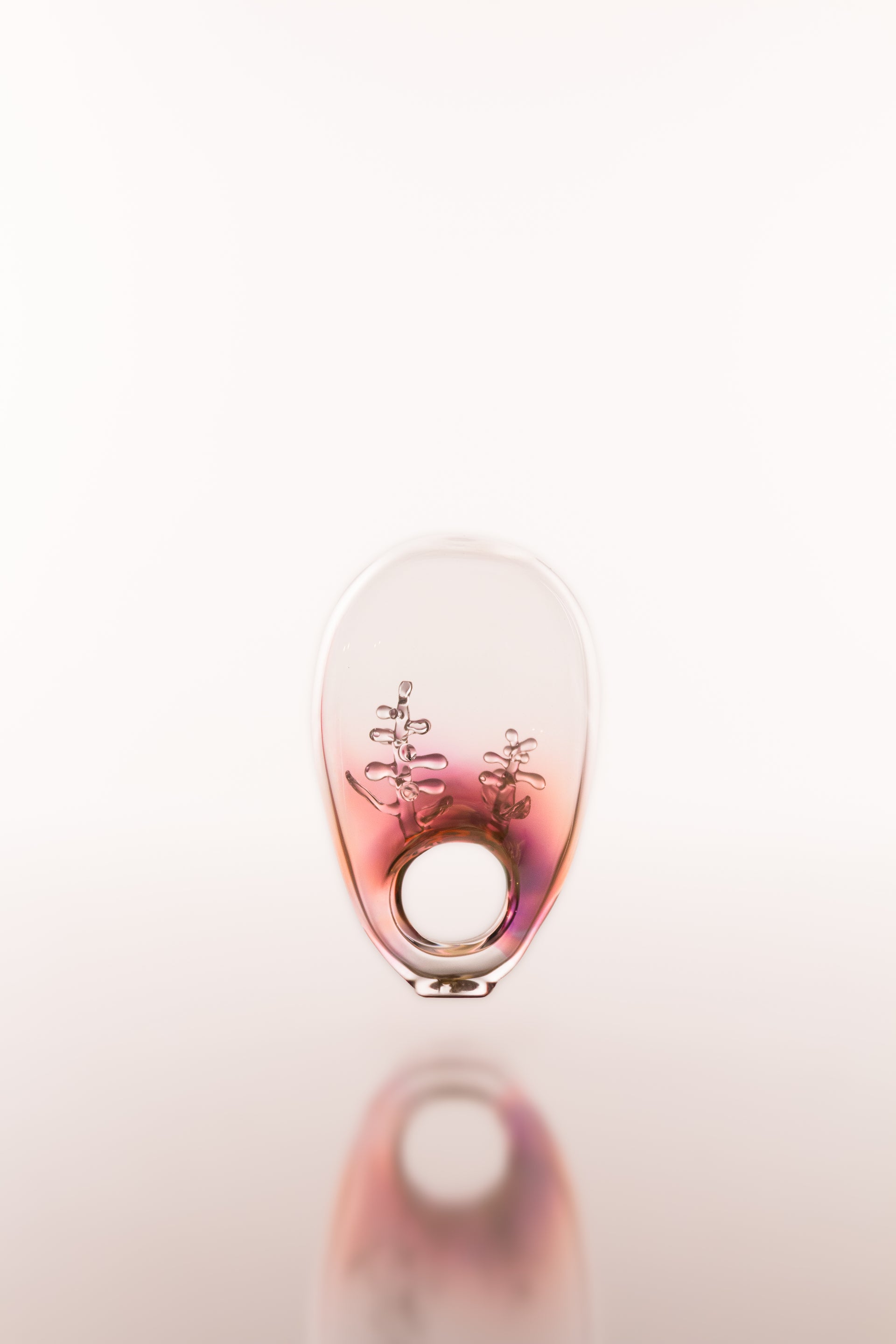 Small round glass object featuring delicate decorative forms inside with a reflective surface on a white background
