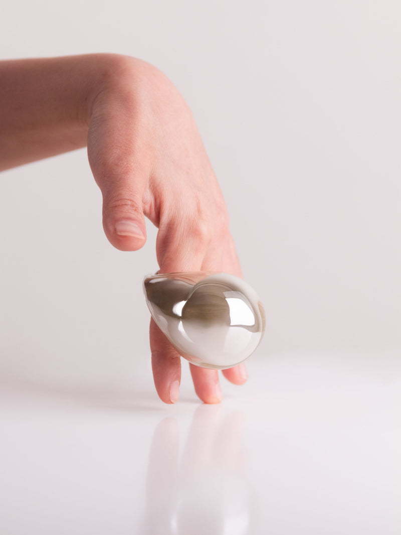 Hand holding a silver teardrop-shaped object against a light background