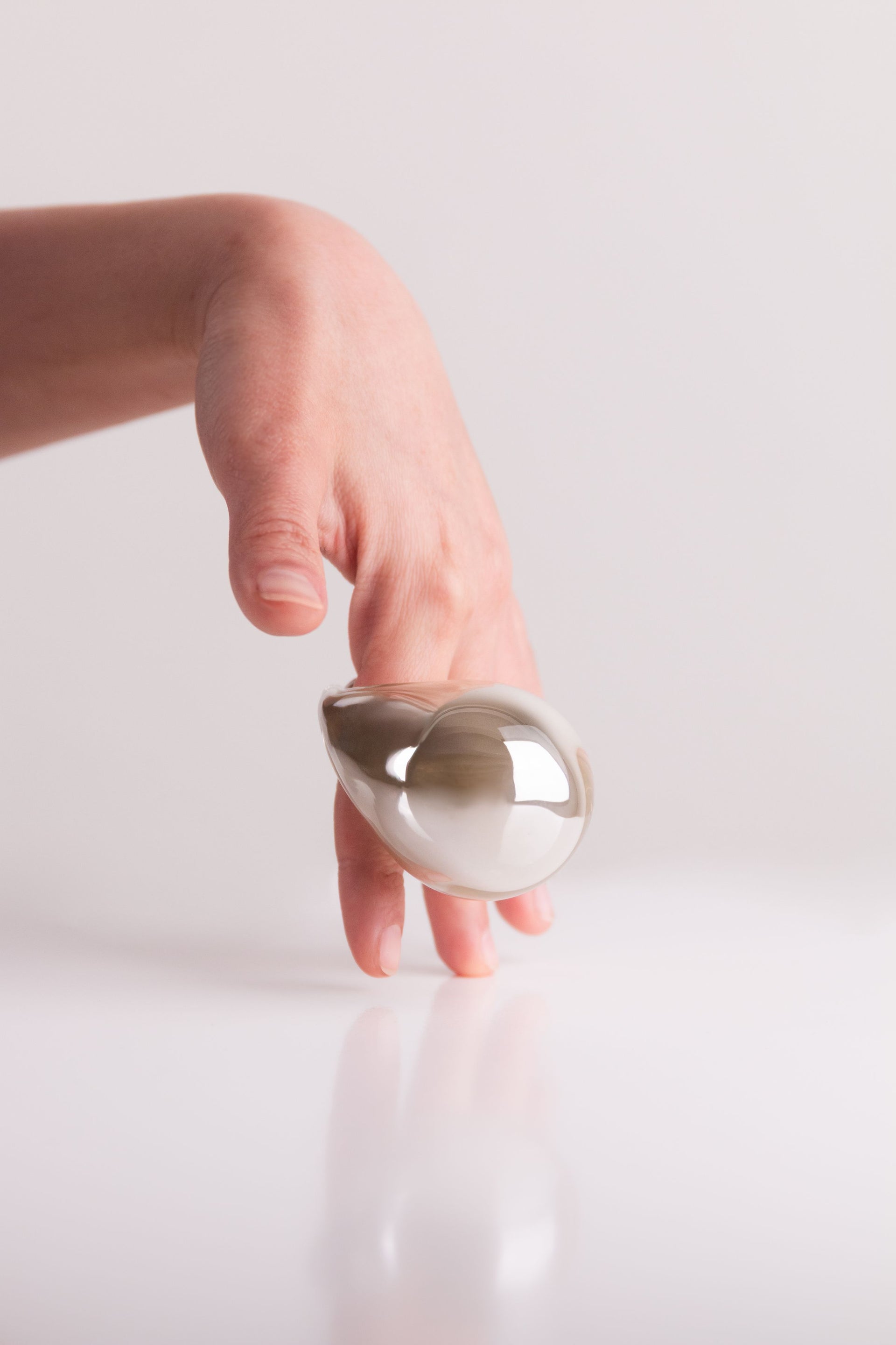 Hand holding a silver teardrop-shaped object against a light background